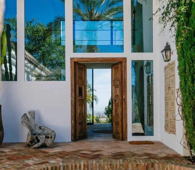Puerta de entrada con grandes ventanales y vista al exterior, rodeada de vegetación.