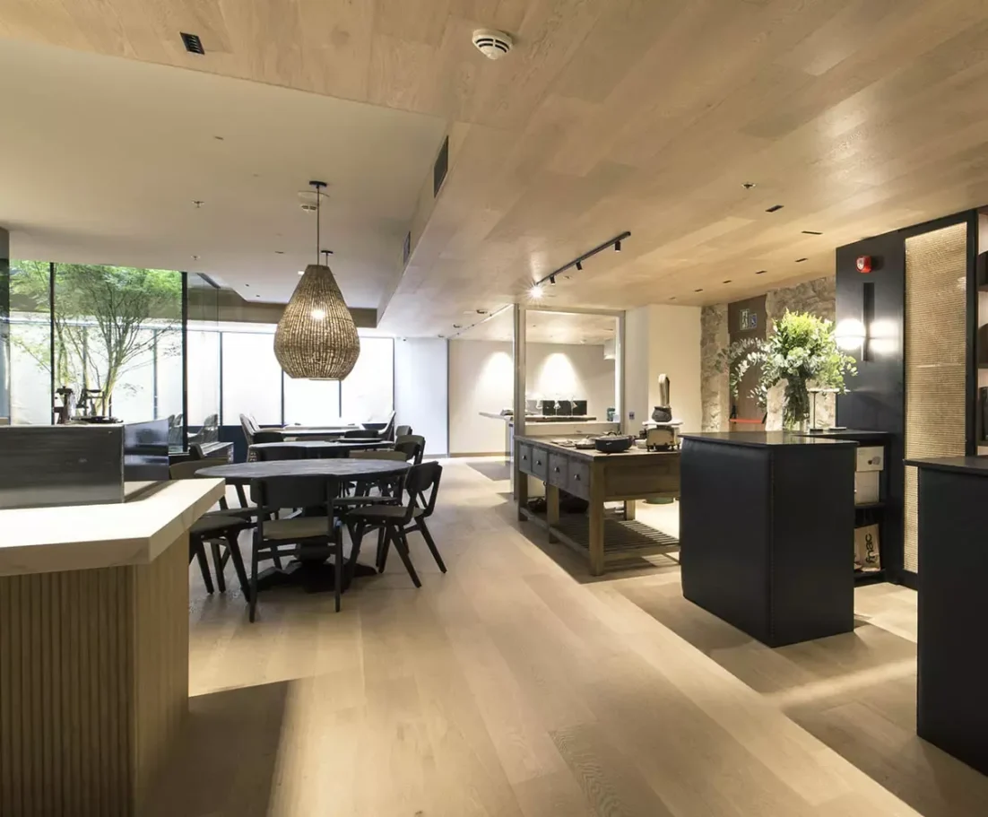 Interior de un restaurante moderno con mesas de madera y iluminación natural.