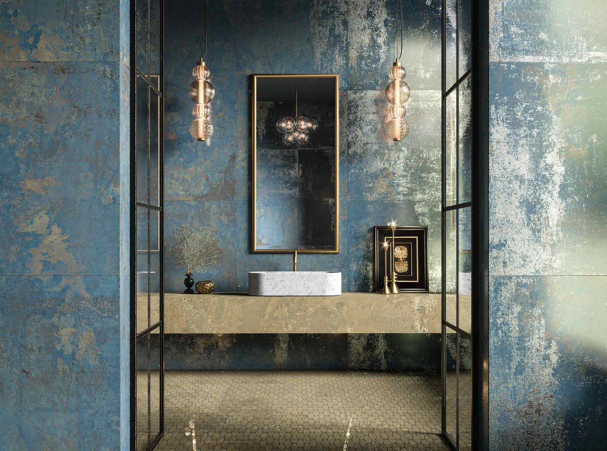 Baño elegante con paredes azules y doradas, espejo enmarcado y lavabo moderno.