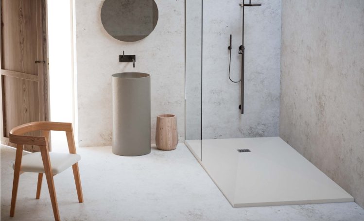 Baño moderno con ducha de vidrio, lavabo cilíndrico y una silla de madera.