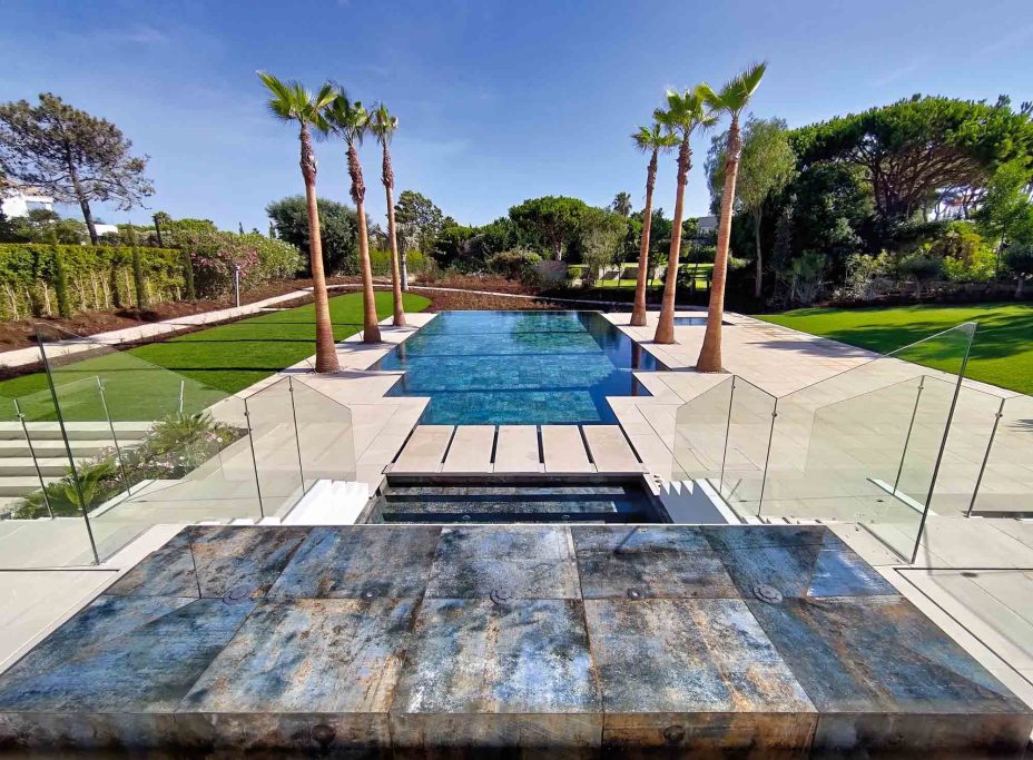 Vista de un elegante patio con piscina y palmeras en un entorno natural.